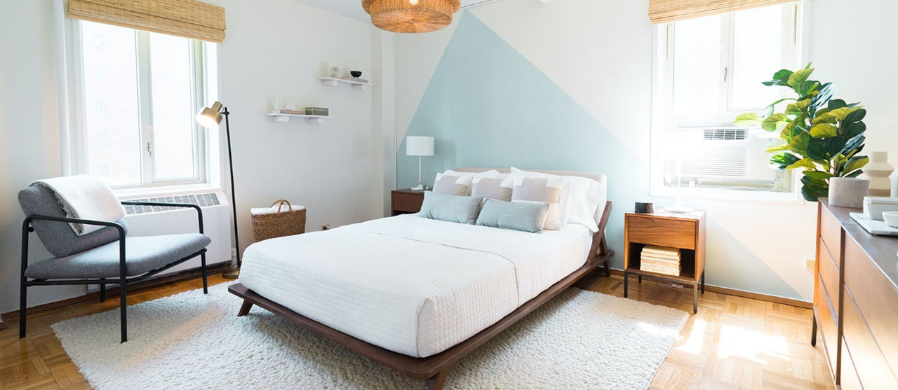 Bedroom with blue triangle statement wall, white bed, plant, ceiling light