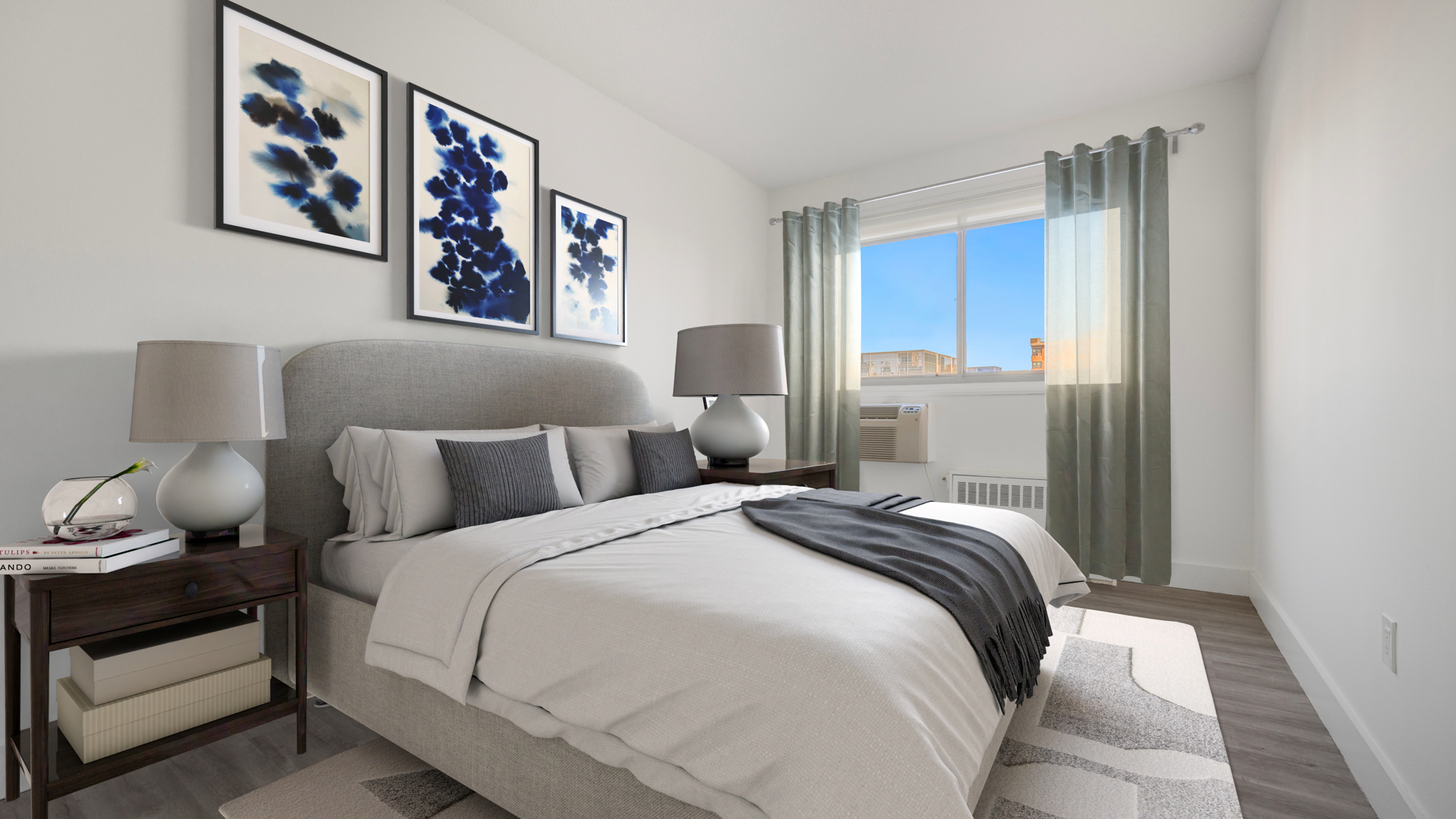 Bedroom with white and gray bedding, dark blue artwork, bedside table